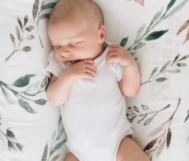 Baby in a white onesie lying on a floral-patterned blanket