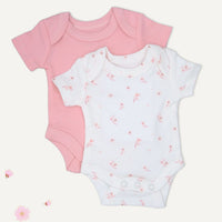 Two short-sleeve baby bodysuits laid flat on a light cream background: one solid light pink and one white with a scattered small pink floral print. No person, animal, or real environment is present.