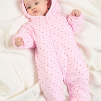A baby lying on a white textured blanket wearing a pink hooded footed sleeper with small dark polka dots.