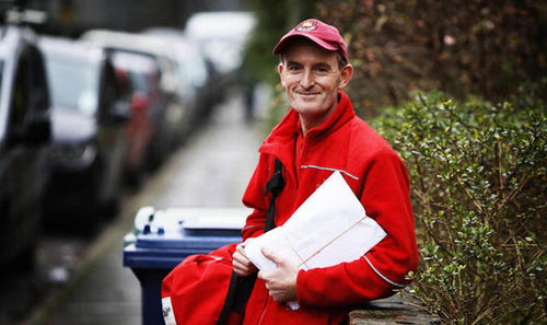 Delivery in red uniform holding a package on a street with cars and greenery in the background