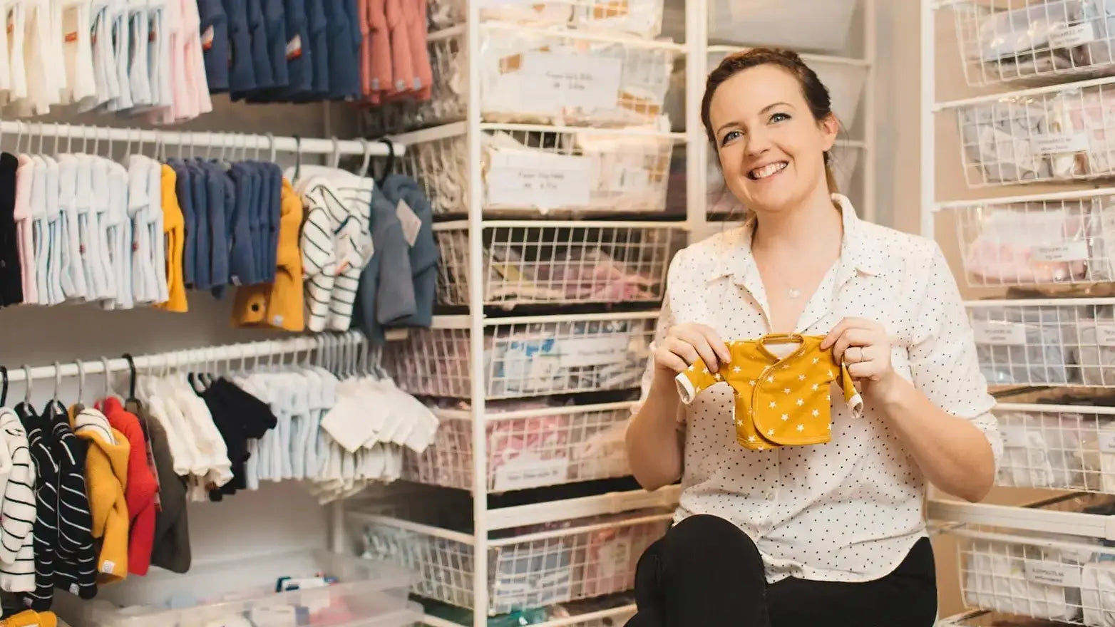 NICU Nurse holding a yellow tiny baby  baby outfit in a store with shelves of clothes in the background