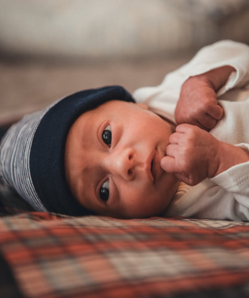 Newborn baby wearing a blue hat lying on a plaid blanket