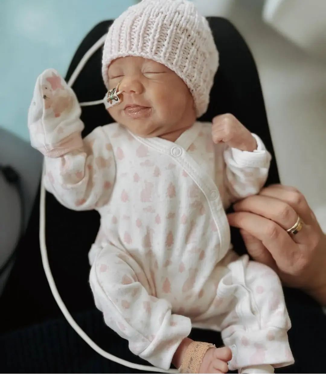 Tiny Newborn baby in a white outfit and knitted hat with medical equipment nearby.