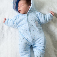Newborn baby wearing a blue onesie with a hood on a white blanket