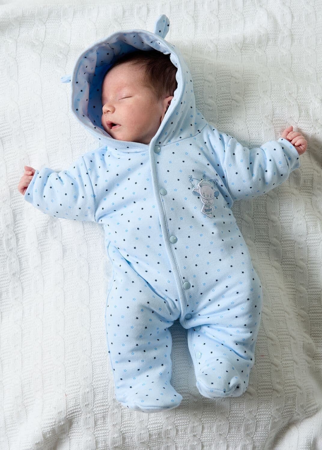 Newborn baby wearing a blue onesie with a hood on a white blanket