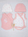 A baby clothing set laid flat on a white textured fabric background, including a pink knit hat, a white knit hat with small pink floral prints, a pink wrap vest, and a white wrap vest with pink trim and tiny pink floral prints. A small dried flower stem lies between the garments.