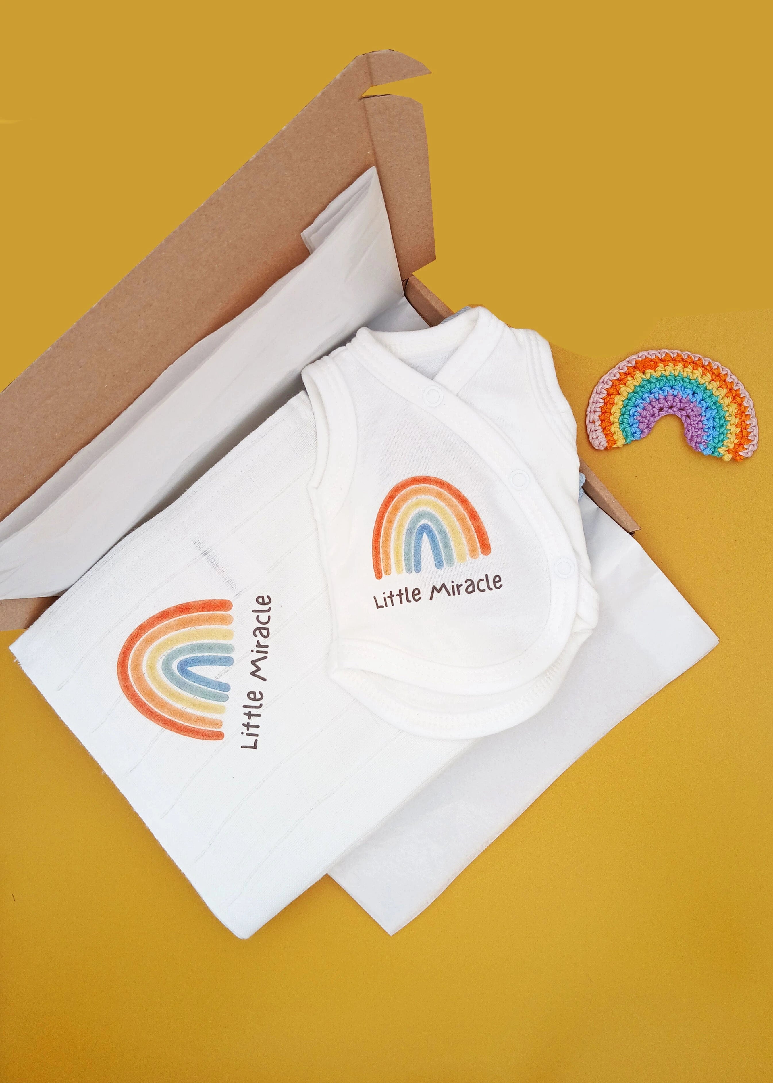 White baby romper with rainbow design and 'little miracle' text on a yellow background