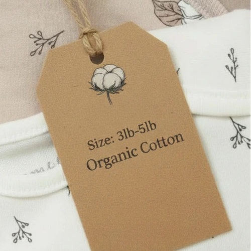 A kraft paper product tag with a cotton boll illustration and the text 'Size: 3lb-5lb Organic Cotton' hanging from a twine loop over a white and blush printed fabric.
