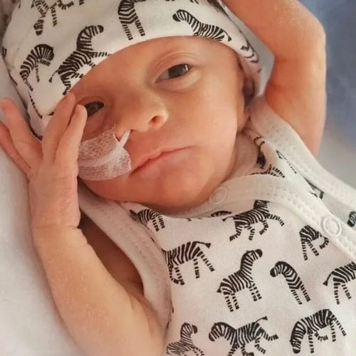Premature Baby wearing a zebra-patterned outfit and hat on a soft surface