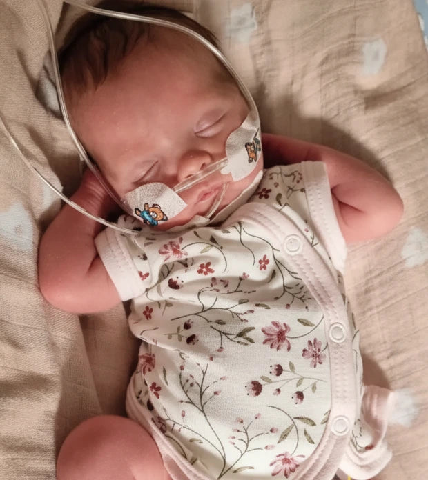 Baby wearing a floral onesie and medical mask, lying on a soft surface.