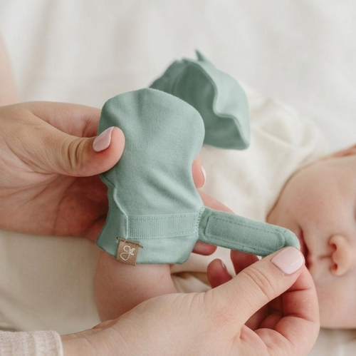 Person holding a pair of light green baby booties with a neutral background