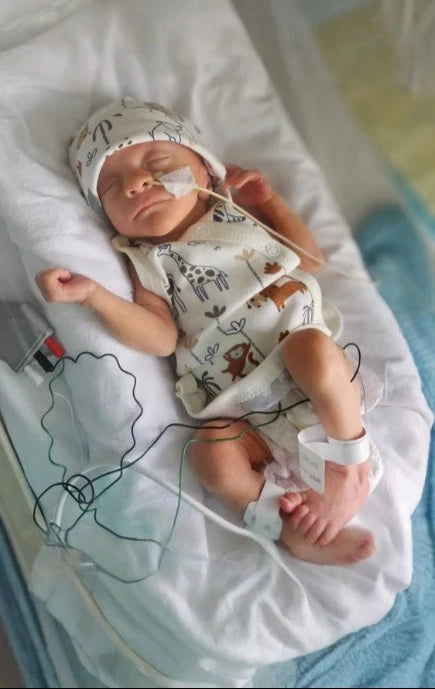 Dressed premature baby, in prem baby clothes, lying in a hospital NICU with medical equipment attached