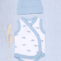 A baby clothing set featuring a white wrap bodysuit with light blue trim and a matching light blue beanie hat, styled flat-lay on a textured light blue background with dried bunny tail grass.
