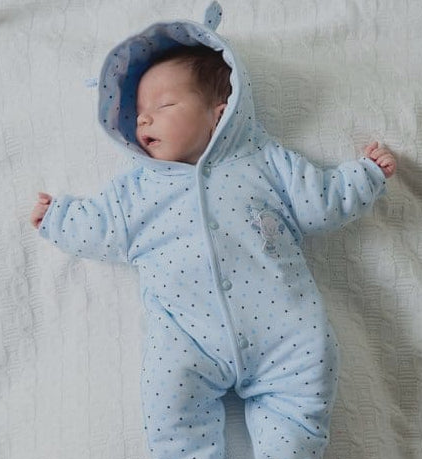 Newborn baby in a blue onesie with a hood on a light background