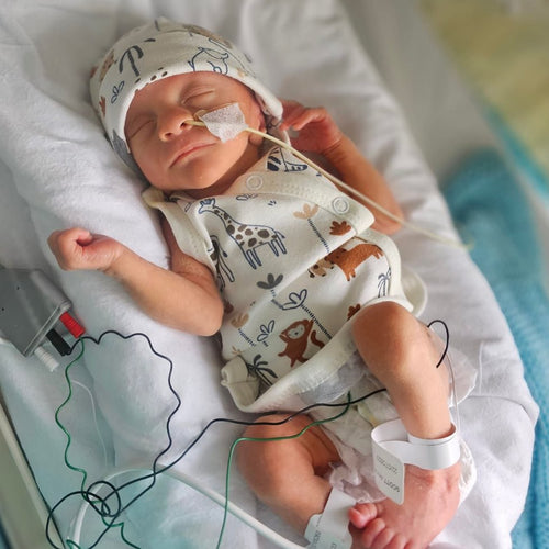 Newborn baby in a hospital setting with medical equipment and wires.