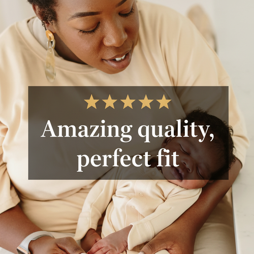 A woman in a cream-colored sweatshirt holds a sleeping newborn baby wearing a matching cream-colored bodysuit. The woman is wearing a gold-toned statement earring and a smartwatch.